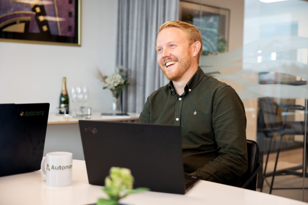 Medarbetare på Autonomi sitter framför datorn och ler medans han hjälper en utav sina småföretagare med ekonomin.